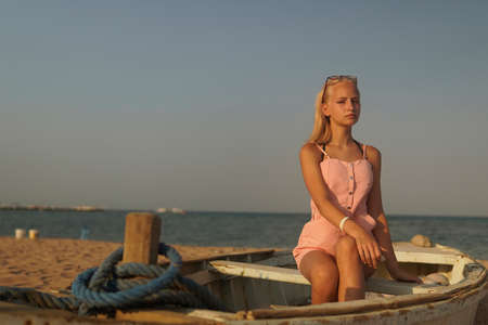 teenage girl with blonde hair sit on an old boat to the shore of the seaの写真素材