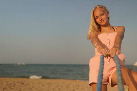 girl teenager with blonde hair pull a rope and laugh on the shore of the sea.の写真素材