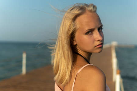 girl teenager with blonde hair stand on the pier of the sea.の写真素材
