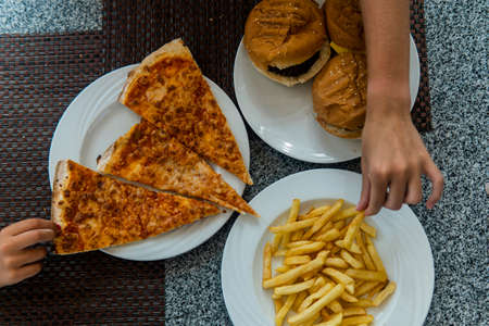 children's hands to take fast food on the table. Pizza, hamburger, fries.の写真素材
