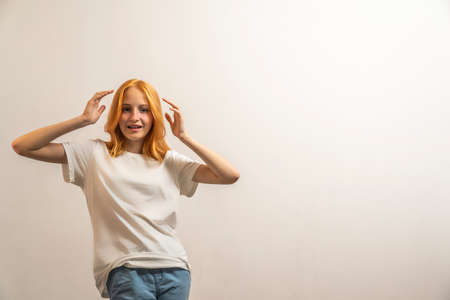 Portrait of a teenage girl with red hair and a white T-shirt on a light background.の写真素材