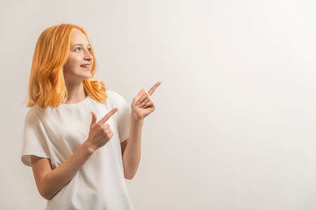Portrait of a teenage girl with red hair and a white T-shirt showing up on a light background.の写真素材