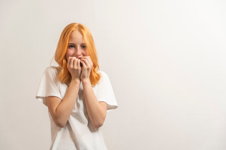 Portrait of a teenage girl with red hair and a white T-shirt to fear on a light background.の写真素材