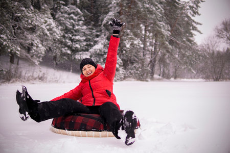 a girl in a red jacket rides a tubig in a snowy forest and laughsの写真素材