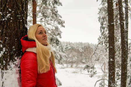 portrait of a blonde girl in a red jacket in a snowy forest