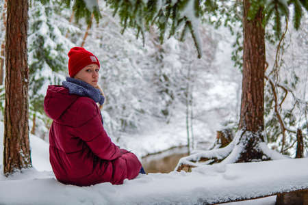 teenage girl sit on a bench in a snowy forest bench.の写真素材