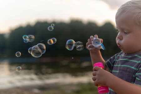 little boy blowing soap bubbles by the lake in the park.の写真素材
