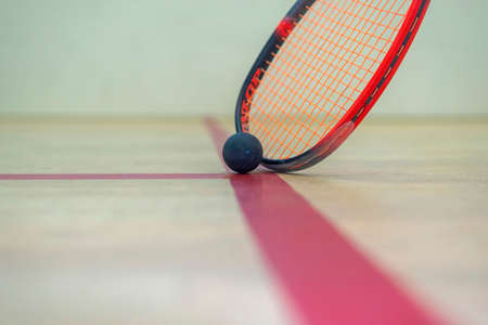 the squash racket and ball lie on the wooden floor between the lines dividing the squash zones.の写真素材