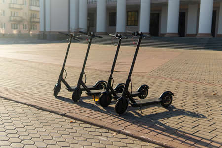 electric scooters stand in the city near the building with columns in the rays of the autumn sun.