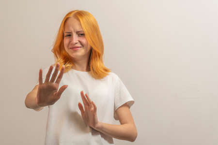 teen girl with red hair in a white t-shirt on a light background hands forward say no.の写真素材