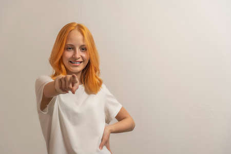 teen girl with red hair in a white t-shirt on a light background point finger forward.の写真素材