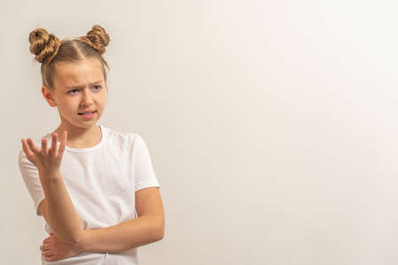 teenage girl with dark hair hair in a white t-shirt on a light background frown eyebrows and think.の写真素材