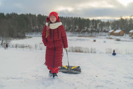 a girl in a red jacket walks down a snow-covered slide with tubingの写真素材