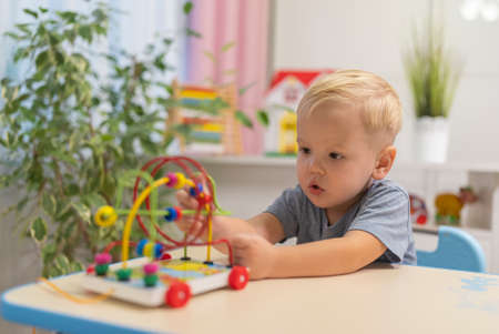 little boy child blonde play with toy to sit at the table at homeの写真素材