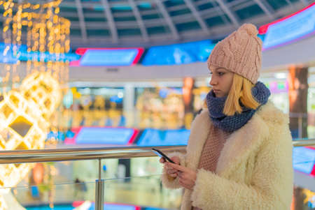 teenage girl in white jacket shopping mall watch phoneの写真素材