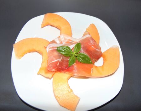 Ham and melon with basil on a light dish on a gray background. Italian Cuisine.の写真素材