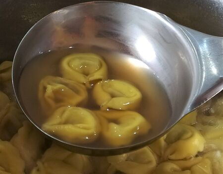 Italian tortellini (Tortellini al brodo) in meat broth in a soup ladle, close up.の写真素材