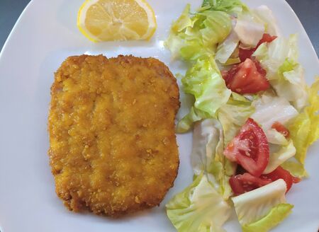 Italian cutlet milanese (cotoletta alla milanese) with lemon and fresh salad on the light plate,...