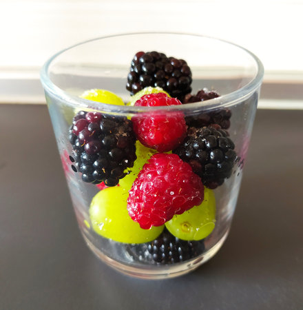 Mixed berries, raspberries, blackberries and grapes in a glass on gray background. close-up. Berry salad Macedonia, dessert, Italy.の写真素材