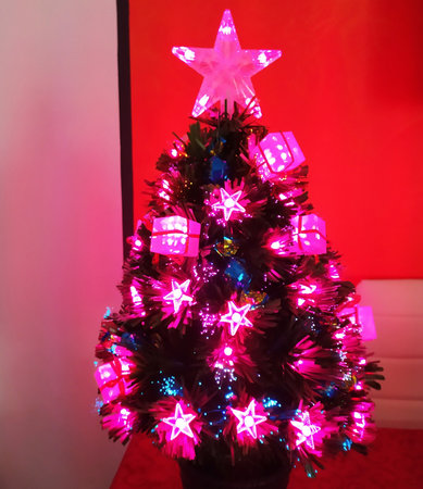 Christmas tree decorated with colorful pink lights at night on a red background with copy spaceの写真素材
