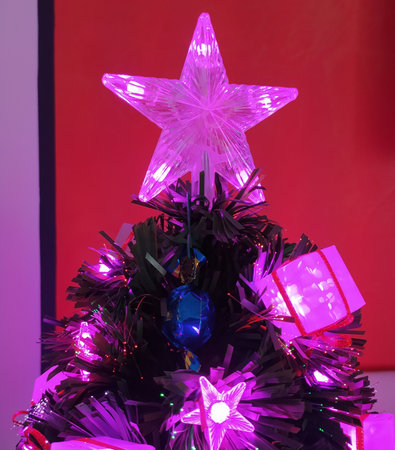 Christmas pink star on a Christmas tree decorated with pink and purple lights and ribbons on a red background at nightの写真素材