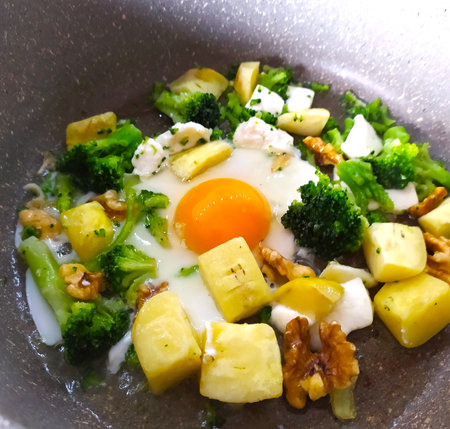 Fried eggs with broccoli, potatoes and walnuts in a pan, close-up, isolated, vegetarian breakfast, cooking, healthy eating.の写真素材