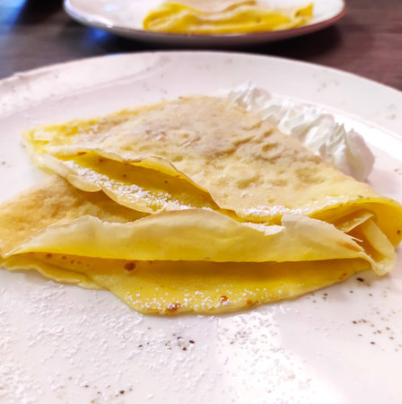 Crepes with whipped cream on a plate, close-up. Crepes stuffed with whipped cream and powdered sugar...