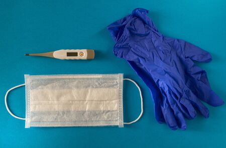 A medical mask, medical gloves and a thermometer on the blue surface. Concept coronavirus, flu,...