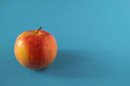One yellow-red ripe apple on a blue background. View from the front. Horizontal orientation.の写真素材