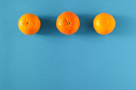 Three ripe juicy tangerines are laid out on a blue surface in a line. Horizontal orientation. Copy space.の写真素材