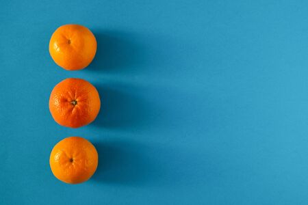 Three ripe juicy tangerines are laid out on a blue surface in a line. Horizontal orientation. Copy space.の写真素材