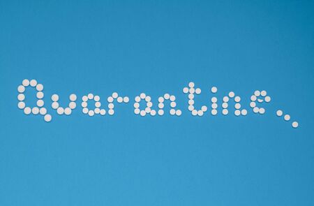 The word quarantine, laid out with white tablets on a blue background horizontally. Coronavirus, quarantine concept. Selective focus. Horizontal orientation. View from above.の写真素材