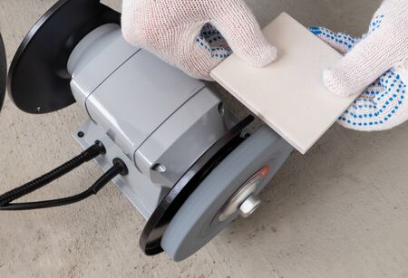 The hands of the master in white construction gloves hold a tile or porcelain tile, which is...