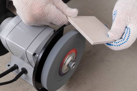 The hands of the master in white construction gloves hold a tile or porcelain tile, which is...