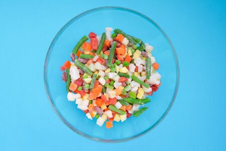 Shredded frozen vegetables in a glass bowl on a blue background. Horizontal orientation. View from above.の写真素材