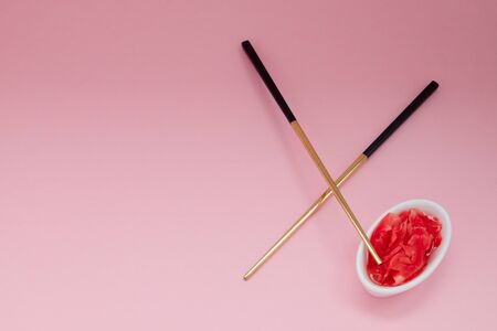 Marinated ginger and chopsticks with black handles, folded cross on a pink background. Flat lay with copy space, selective focus. Japanese food. Horizontal orientation.の写真素材