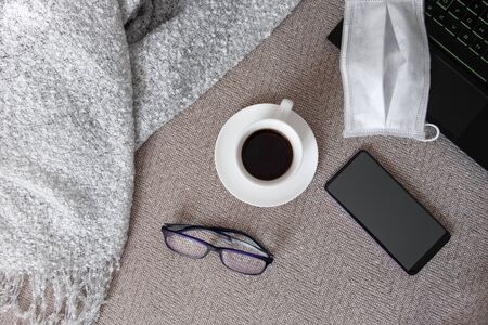 A laptop, a medical mask, glasses and a smartphone on a sofa with a plaid. Work or study from home, self-isolation, protection from coVID-19 concept. Horizontal orientation.Selective focus.の写真素材