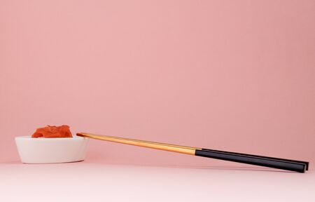 Marinated ginger and chopsticks with black handles, folded cross on a pink background. Flat lay with...