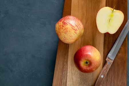 Knife with a wooden handle, two whole apples and one half lie on the cutting board. Healthy food,...