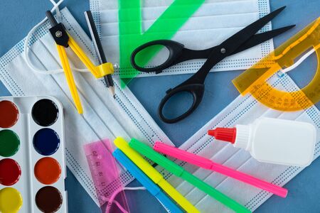 School supplies and three medical masks on a blue background. Back to school, the pandemic coronavirus concept. Horizontal orientation. Selective focus. View from above.の写真素材