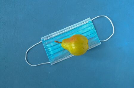 Close-up medical mask and pear against a blue background. A symbol of a pandemic, the protection of...