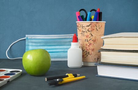 Books, apple and stationery for study. The medical mask as a symbol of covid-19 in the background....