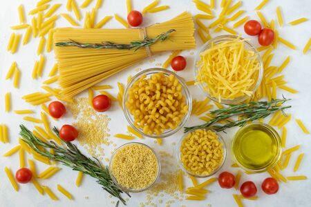 A variety of pasta, cherry tomatoes, olive oil and rosemary on a light surface. Italian cuisine,...