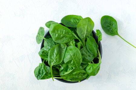 Fresh spinach leaves in a black bowl on a light surface. Fresh greens. Vegetarianism, healthy eating...