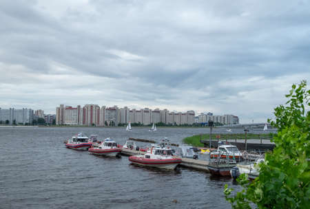 St. Petersburg, Russia. July 04, 2020. Rescue boats on the pier on the river against the background of residential areas on the other side in cloudy weather. Horizontal orientation, selective focus.のeditorial素材