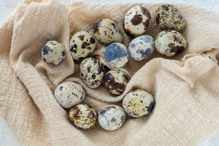 Close up many fresh quail eggs lie on a light linen napkin. Horizontal orientation, top view....