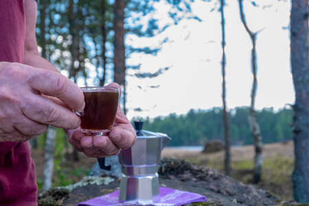 Hands of an adult middle-aged man hold a small glass cup of coffee against the background of the...