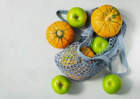 Small ripe pumpkins and green apples in an ecological string bag. The concept is plastic free, environmental protection, healthy lifestyle. Horizontal orientation, top view, copy spaceの写真素材