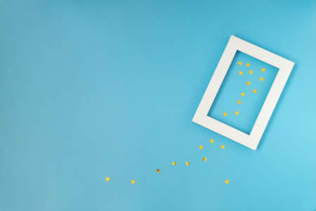 Close-up of empty white frame on blue background with confetti. Celebrating Christmas, New Year. Horizontal orientation, selective focus, top view. Mockup.の写真素材