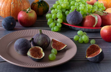 Ripe fresh figs, grapes, apples and pumpkins on a table with a wooden surface. Harvest, autumn...